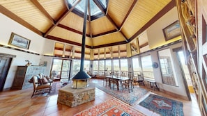 A spacious interior with a high ceiling, large windows, a stone fireplace, and a dining area. - Views | Pet Friendly | Folley Cabin (Angel Fire)