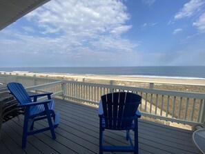 Um deck de madeira com duas cadeiras Adirondack azuis voltadas para a praia.
