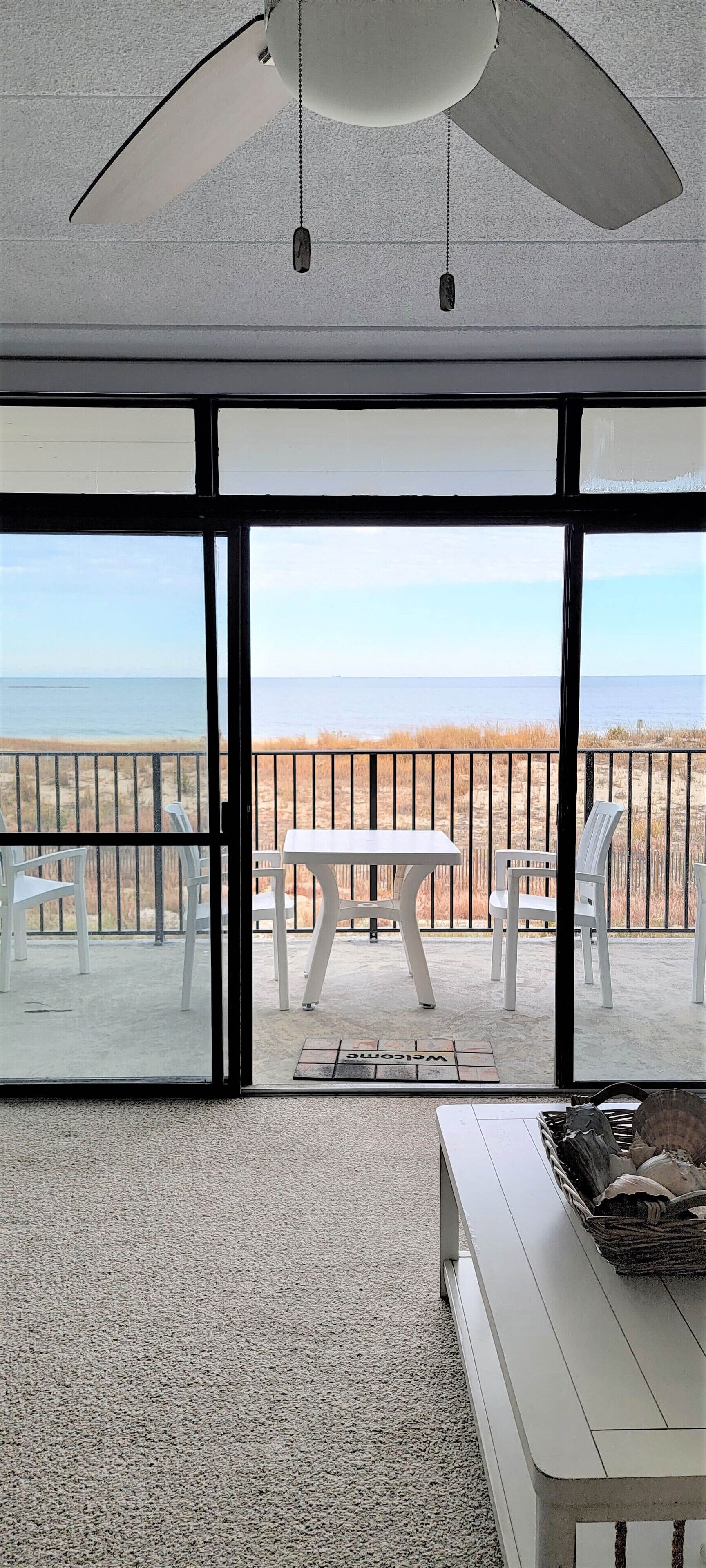 A room with a large sliding glass door leading to a balcony with a view of the beach and ocean.