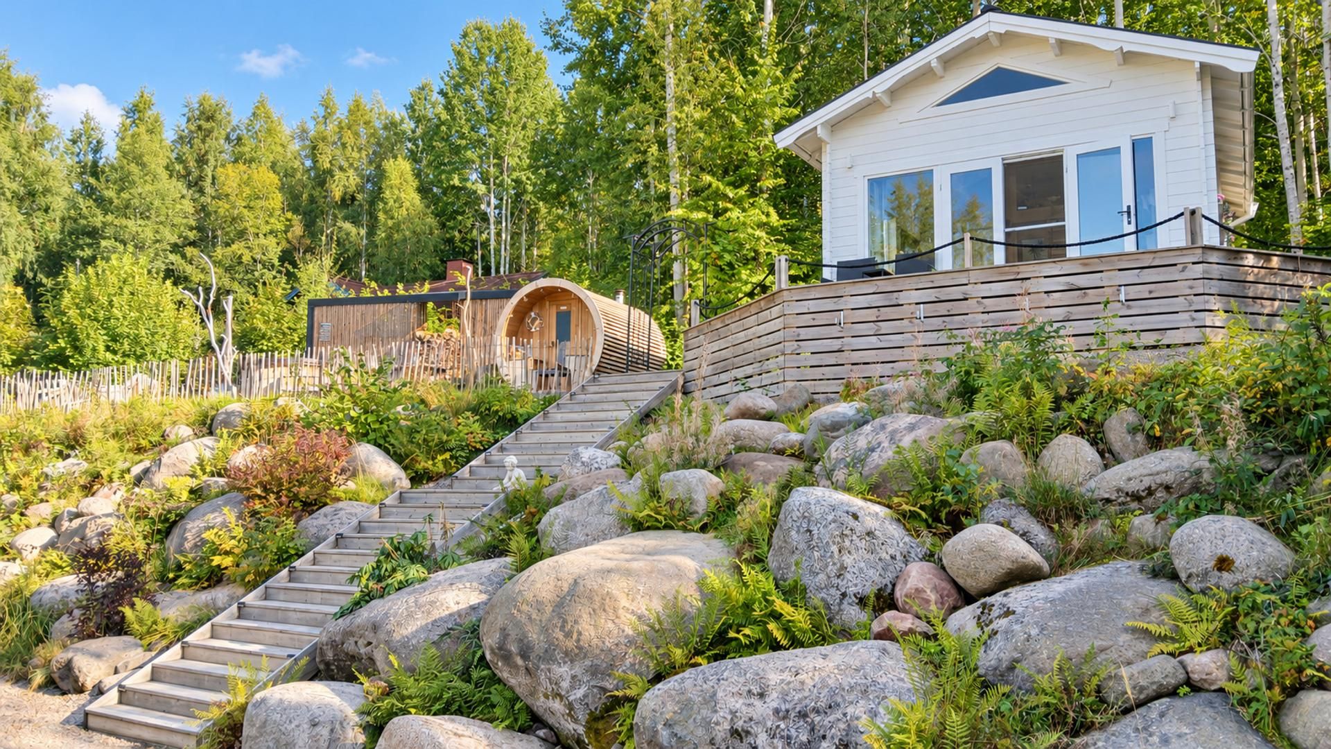 Una cabaña con escalera de madera que lleva a una puerta, rodeada de grandes rocas y follaje.
