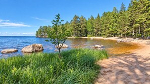 A beach with clear water, rocks, and a forested area.