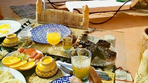 A dining area with a table set for breakfast, including plates, glasses, and a variety of food items. There are lounge chairs and a decorative birdhouse in the background. - Close to everything in the medina - Authentic renovated Moroccan house (Marrakech)