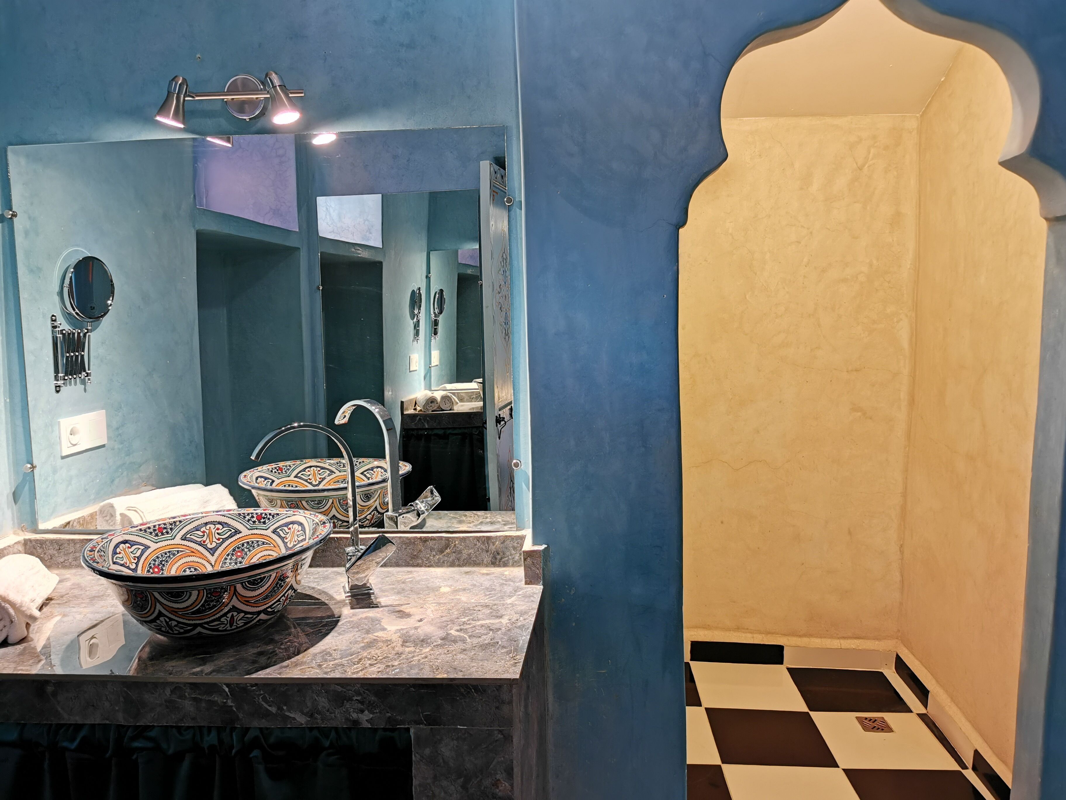 Un bagno con un ampio specchio, un lavabo e una doccia con pavimento a scacchi.