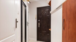Un pasillo con paredes blancas, una puerta de madera oscura y un piso de baldosas claras.