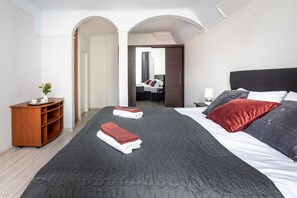 A hotel room with a large bed, a wooden side table, a small plant, and a view of another room through an open door. - Asana Apartament by Dream (Sopot)