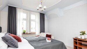 Una habitación de hotel moderna con una cama grande, una mesita de madera y vistas a la ciudad a través de amplios ventanales.