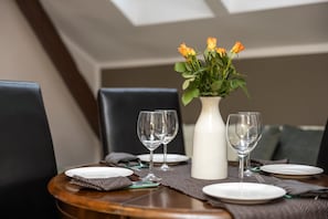 A dining table set with white plates, two wine glasses, and a white vase with yellow flowers. - Asana Apartament by Dream (Sopot)