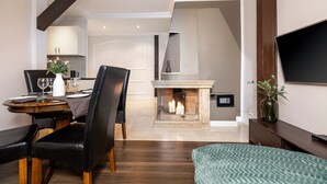 Comedor con una mesa de madera, sillas negras y un jarrón con flores. Se observa una chimenea con velas al fondo.
