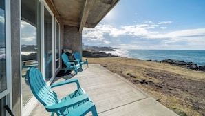 Une vue sur la côte depuis un balcon, avec deux chaises turquoise, un sol en béton et une porte vitrée donnant sur une pièce.