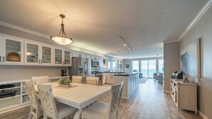 Une cuisine spacieuse avec des meubles blancs, un coin repas doté d’une table et de chaises blanches, et un grand îlot central avec un évier.