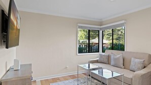 A modern living room with a beige sofa, a glass coffee table, and a flat-screen TV mounted on the wall.