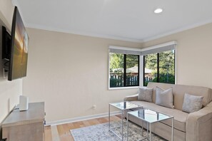 Ein modernes Wohnzimmer mit einem beige farbenen Sofa, einem Glastisch und einem an der Wand befestigten Flachbildfernseher.