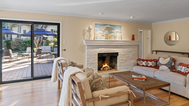 A living room with a fireplace, a sofa, a coffee table, and a view of the outdoor patio.