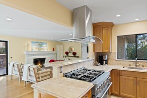 A modern kitchen with a gas stove, wooden cabinets, a fireplace, and a large window.