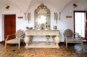 Un área de recepción con puerta de madera, mostrador de recepción, dos sillas, un espejo y piso de piedra.