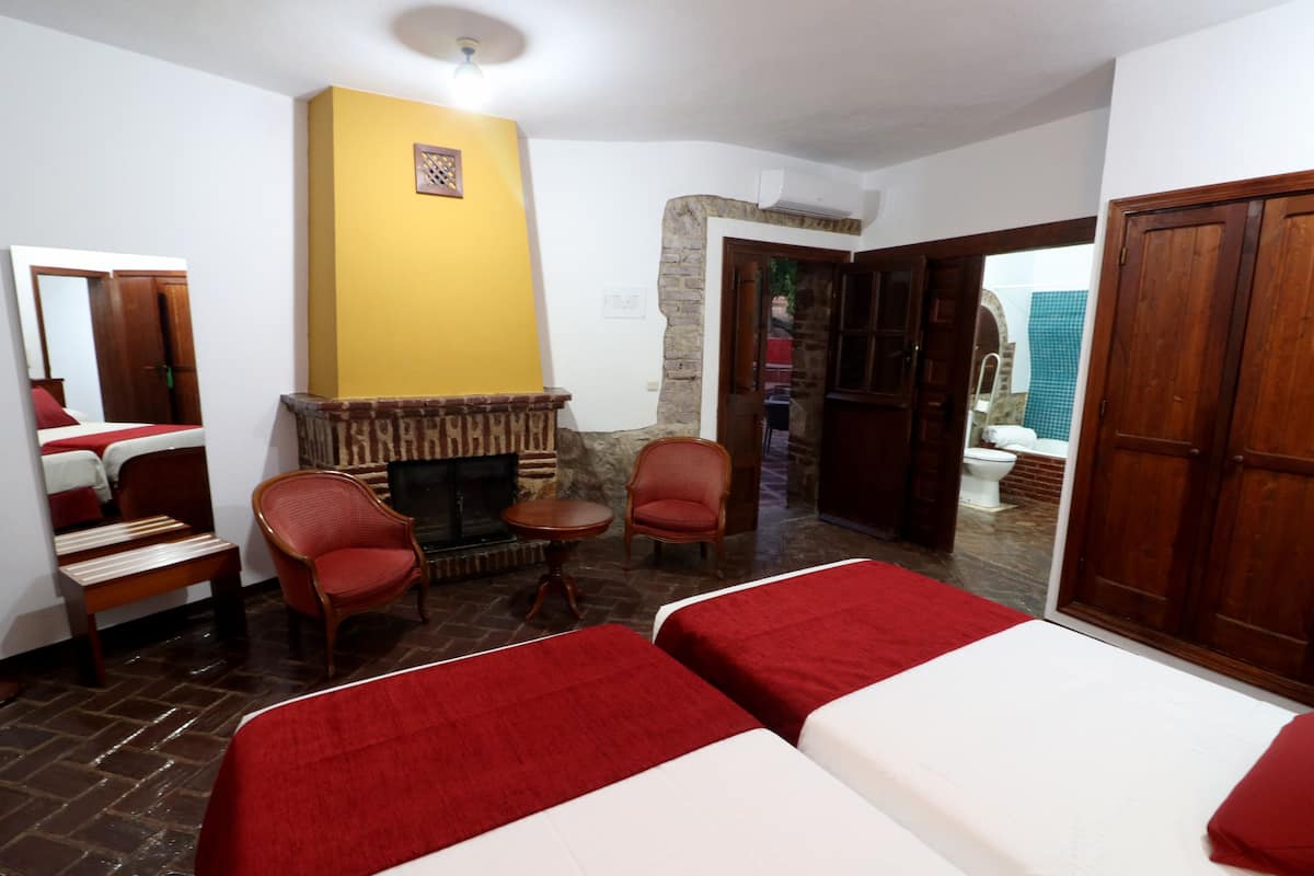 Une chambre d’hôtel avec deux lits, une cheminée, un miroir, une armoire en bois et une vue sur l’extérieur.