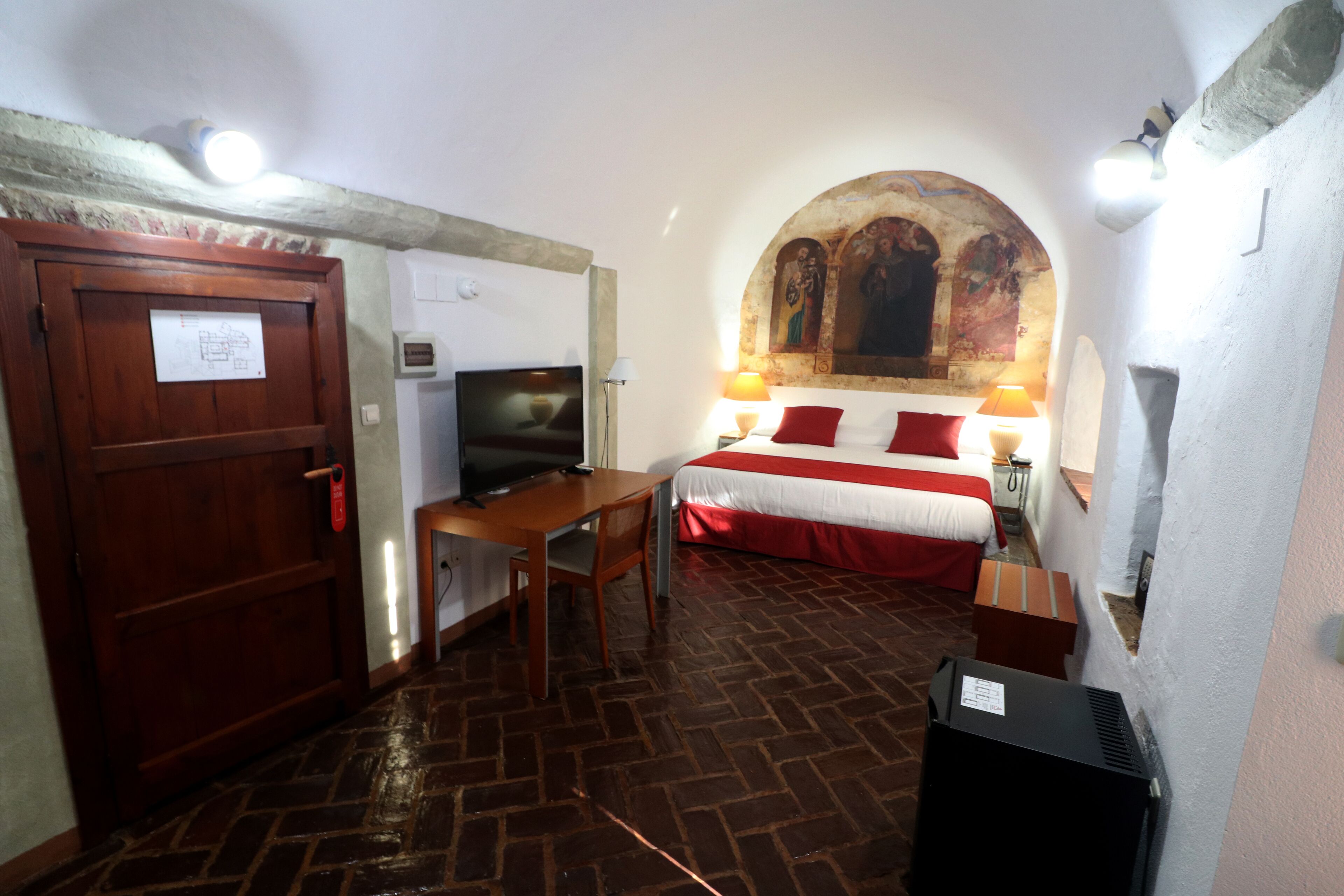 Una habitación con una cama, un escritorio con computadora, televisión y chimenea.