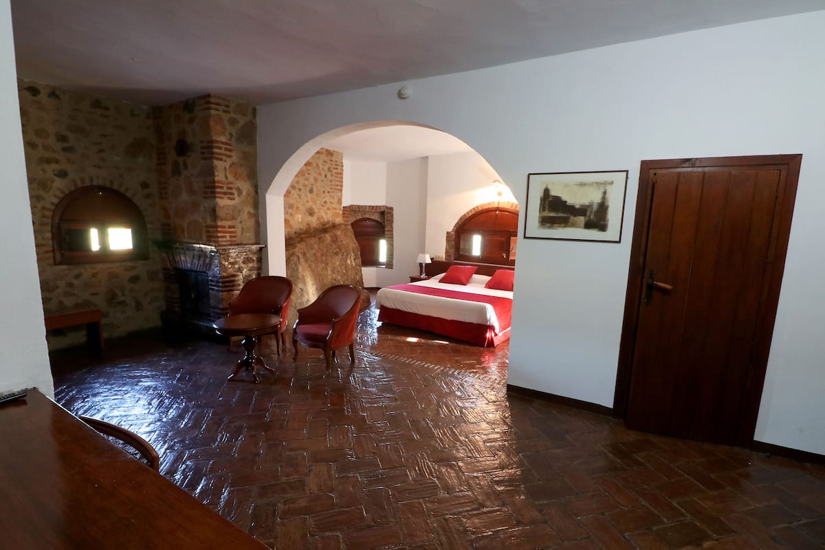 Une pièce avec un mur en pierre, une cheminée, un lit avec une literie rouge et une porte en bois.