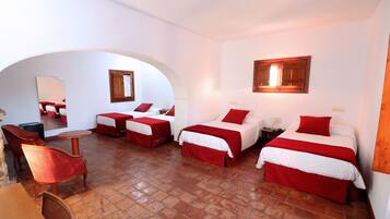 Quarto de hotel com três camas, uma mesa de jantar e cadeiras.