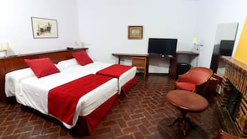 Habitación de hotel con dos camas, un escritorio, televisor y zona de estar.