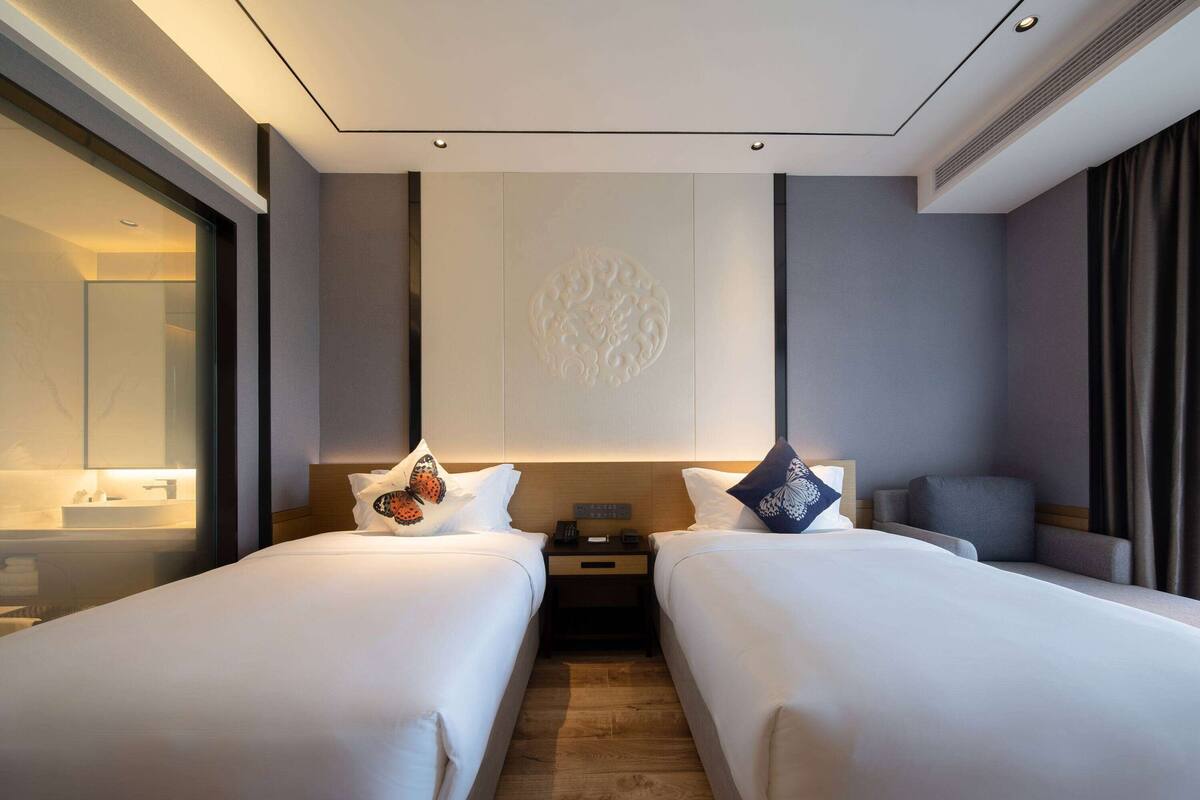 Une chambre d’hôtel avec deux lits, une table de chevet, un miroir et une vue sur l’extérieur.