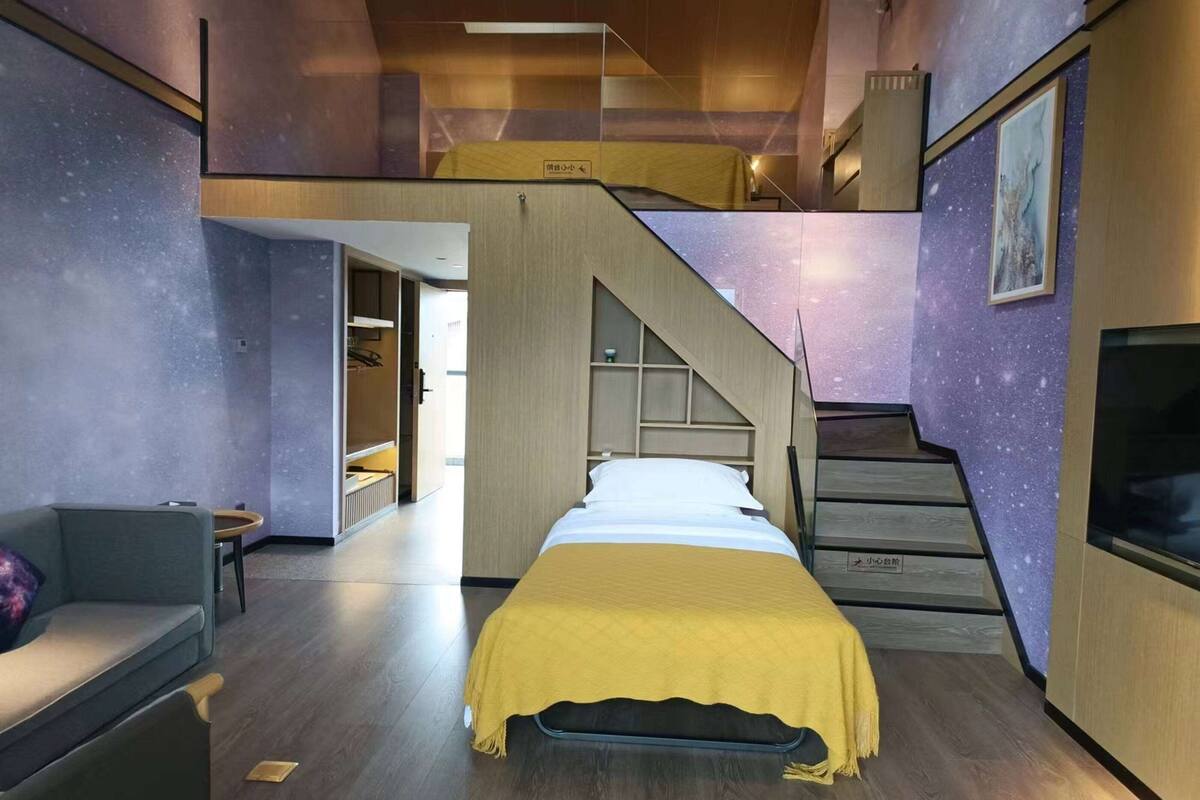 Une chambre d’hôtel moderne avec un lit, un canapé, un escalier et une vue sur le couloir.