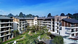 A modern multi-story hotel with a central courtyard, surrounded by lush greenery and mountain views. - Ramada by Wyndham Guilin Yangshuo Resort (Guilin)