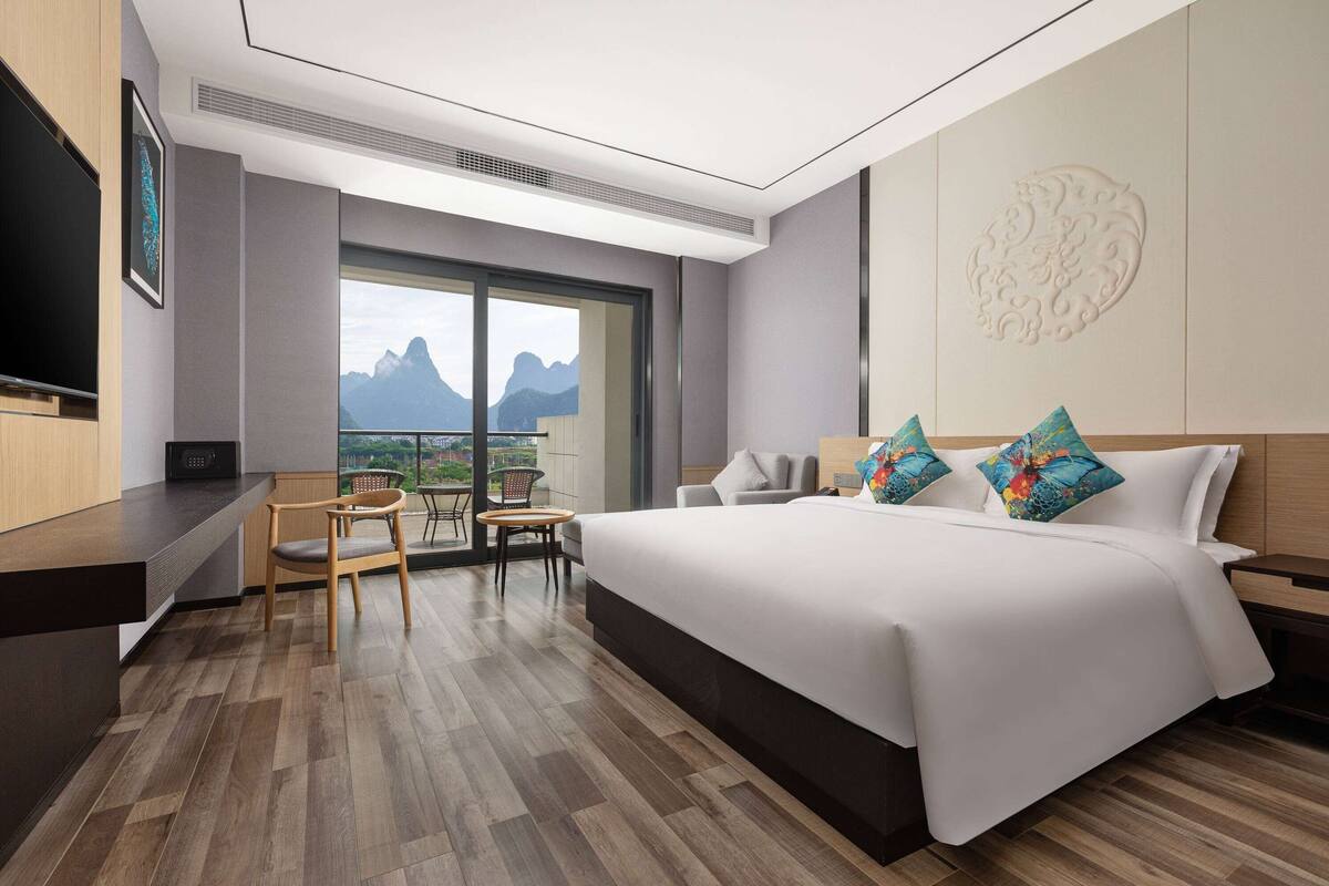 Une chambre d’hôtel avec un grand lit, un bureau, une chaise et une télévision. Il y a une fenêtre avec vue sur la montagne.