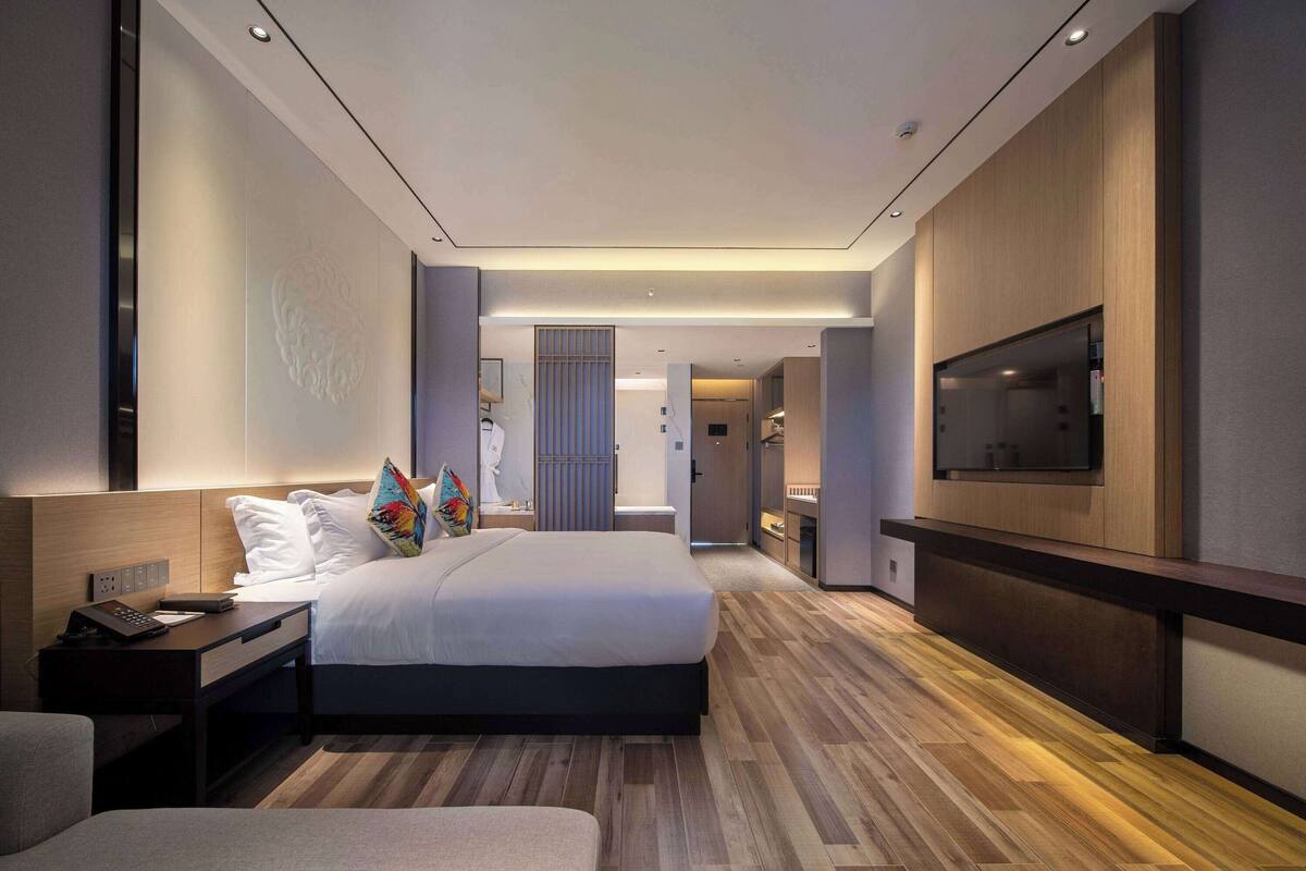 Une chambre d’hôtel moderne avec un grand lit, des tables de chevet, une télévision et un plancher en bois.