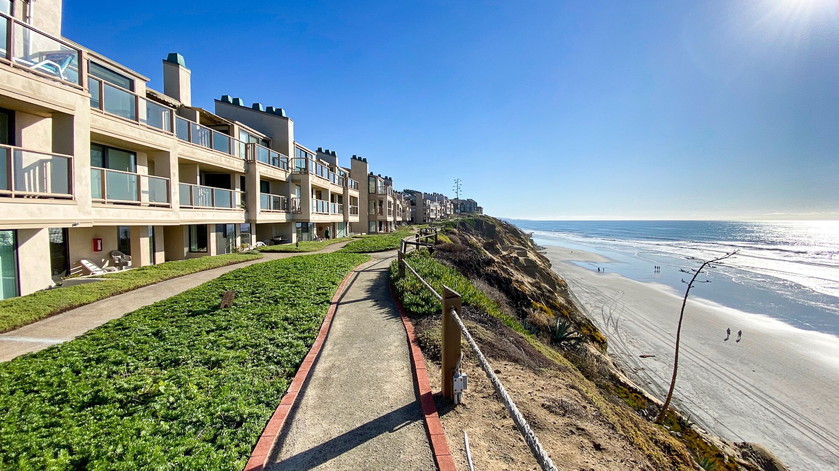 A coastal hotel with multiple balconies, a sandy beach, and a clear view of the ocean.