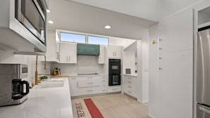 A modern kitchen with white cabinetry, a built-in oven, and a stainless steel refrigerator. - Hacienda Palms - Vacay for 6 - Near Ocean, Pools, Tennis, Racetrack (Solana Beach)
