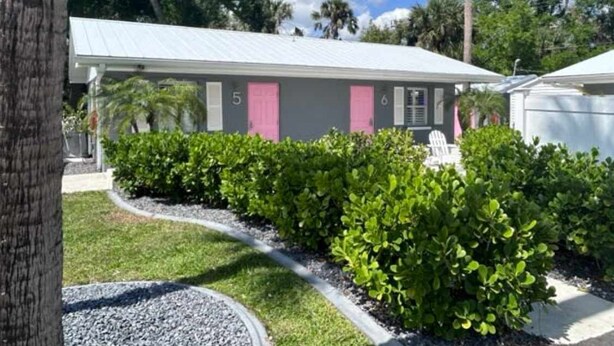 A building with numbered rooms, a covered outdoor area, and a well-maintained garden with shrubs and a gravel path. - Newly Renovated Charlotte Harbor - Sunset Inn #2 (Port Charlotte)