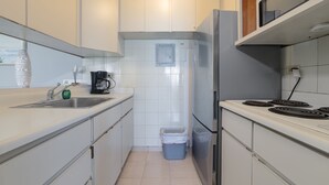 Una cucina compatta con mobili bianchi, un frigorifero in acciaio inox, un fornello e un cestino.