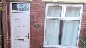 A brick house with a white door and a window with a white blind. - Lovely 2-bed House in Bolton Greater Manchester (Bolton)