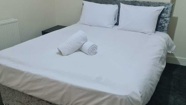 A neatly made bed with white linens and a rolled towel, a dark headboard, and a radiator in the background. - Lovely 2-bed House in Bolton Greater Manchester (Bolton)