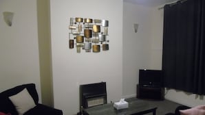 A living room with a fireplace, a television, and a wall-mounted decorative piece. - Lovely 2-bed House in Bolton Greater Manchester (Bolton)
