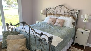 Ein Schlafzimmer mit einem Metallbettgestell, floralem Bettzeug, einem grünen Sessel und einem Nachttisch mit Lampe.