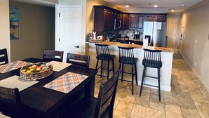 A modern kitchen with dark wooden cabinets, a stainless steel refrigerator, and a central island with bar stools.