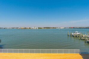 A waterfront view with a wooden dock extending into calm water, a clear sky, and buildings in the distance.
