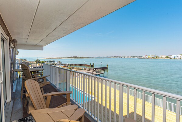 A balcony with a view of the water, wooden chairs, and a table.