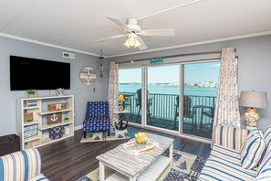 A living room with a television, a ceiling fan, a large window with a view of the sea, and nautical-themed decor. - One of a Kind Direct Bay Views From This 3 Bedroom Condo at Assateague House! (Ocean City)