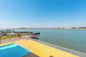 A wooden deck with a pool, a pier extending into the water, and a distant shoreline with buildings. - One of a Kind Direct Bay Views From This 3 Bedroom Condo at Assateague House! (Ocean City)