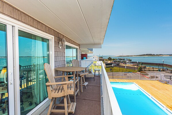 A balcony with a pool, wooden chairs, and a view of the ocean. - One of a Kind Direct Bay Views From This 3 Bedroom Condo at Assateague House! (Ocean City)