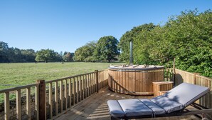 Una terraza de madera con jacuzzi y sillones de descanso con vistas a un campo cubierto de césped.