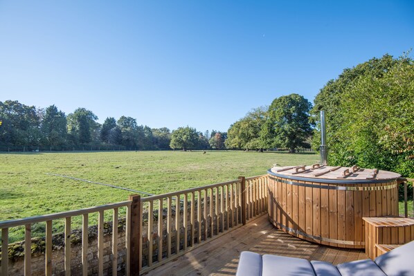 Una terraza de madera con un jacuzzi y vistas a un campo cubierto de hierba.
