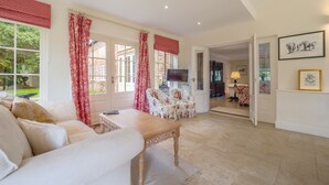 Un salón amplio con un sofá, una mesa de centro y un televisor. Hay una puerta que da a otra habitación y una ventana con cortinas.