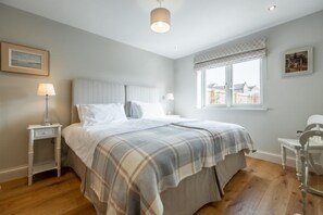 A bedroom with a bed, bedside tables, a window with curtains, and a view of houses outside. - Reenroe, Docking, Norfolk (Docking)