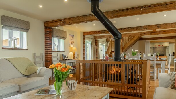 A cozy living room with a fireplace, wooden beams, and a dining area. - The Big Barn (6), Snettisham, Norfolk (Snettisham)