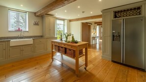 A kitchen with wooden flooring, a wooden table with baskets, a stainless steel refrigerator, and a window with a plant on the windowsill. - The Big Barn (6), Snettisham, Norfolk (Snettisham)