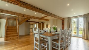 A spacious dining area with a wooden staircase, a large table set for six, and a view of the outdoors through a glass door. - The Big Barn (6), Snettisham, Norfolk (Snettisham)